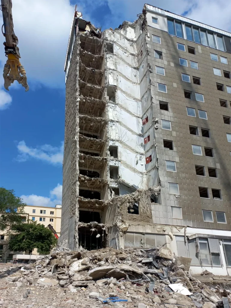 Gebäudeabbruch, bei dem ein Teil der Fassade entfernt wurde und die internen Strukturen sowie eine große Menge Bauschutt sichtbar sind.
