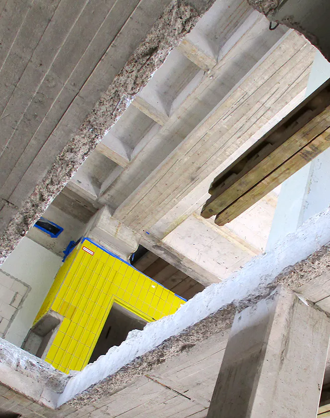 Eine große Baugrube auf einer Baustelle, mit sichtbarer Bewehrung und im Hintergrund stehenden Gebäuden, während Erdarbeiten durchgeführt werden.