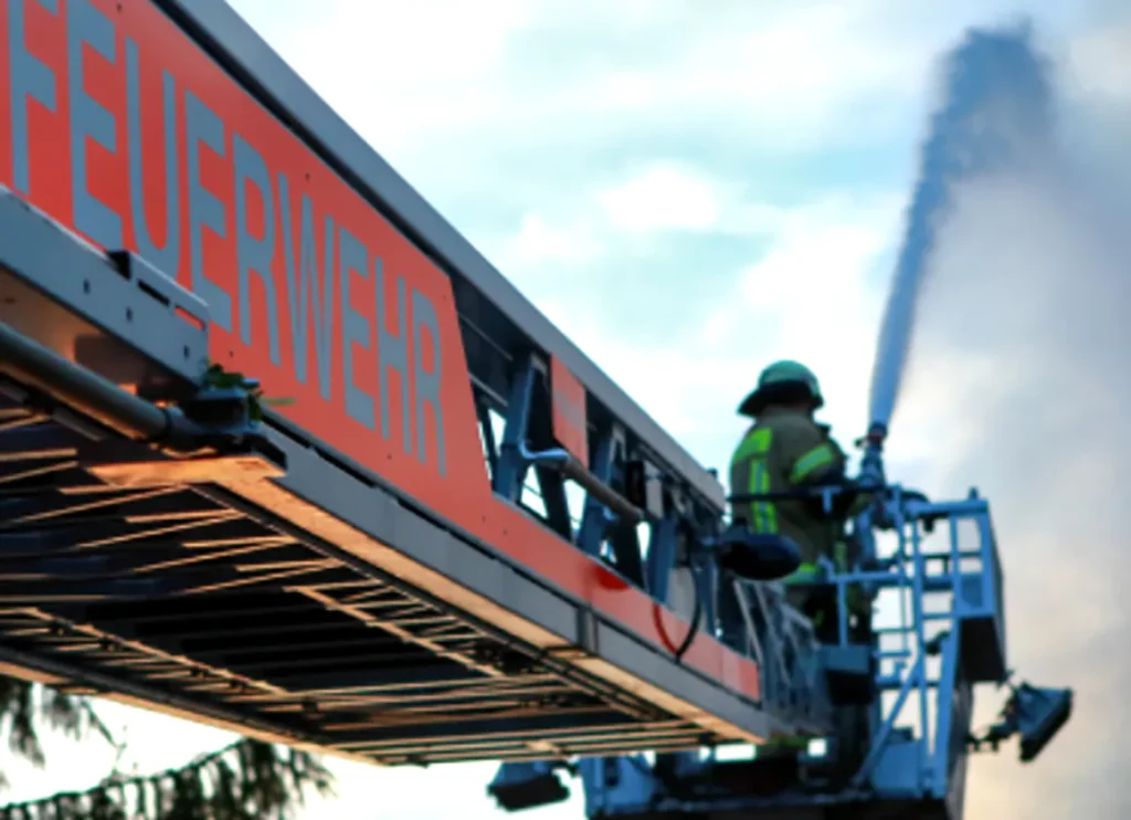 Feuerwehrmann auf Drehleiter löscht Brand mit Wasserstrahl.