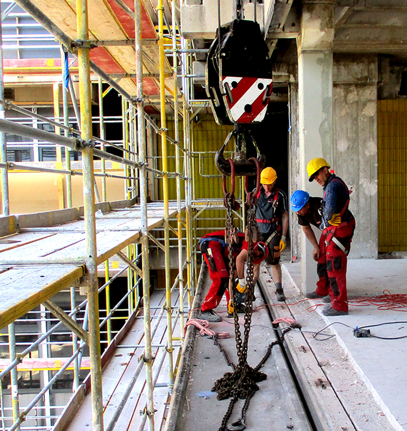 Zwei Bauarbeiter in Schutzkleidung befestigen eine große Metallkette an einem Kranhaken auf einer Baustelle, zeigt Job und Karriere im Baugewerbe.